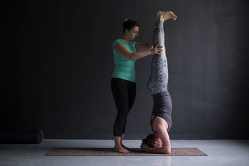 yoga instructor helping female student with headstand pose, salamba sirsasana