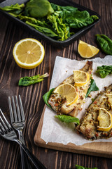 Baked pollock fillet with lemon and spinach on a wooden background