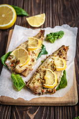 Baked pollock fillet with lemon and spinach on a wooden background