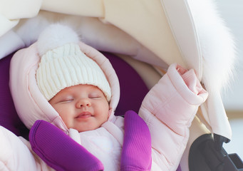 beautiful newborn baby girl sleeping peacefully in pram during a winter walk