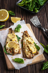 Baked pollock fillet with lemon and spinach on a wooden background
