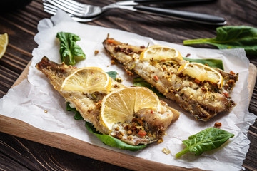 Baked pollock fillet with lemon and spinach on a wooden background
