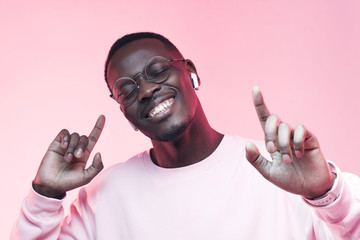 Portrait of young african man listening music with wireless earphones, dancing