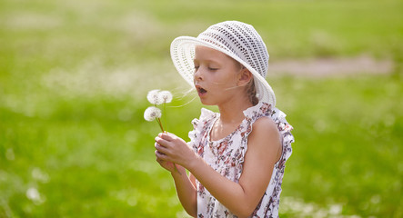 Girl in hat blowing blowball at field