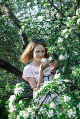 Beautiful close-up portrait of a young elegant red-haired curly woman with hat in tree with white apple-tree cherry tree blossoms