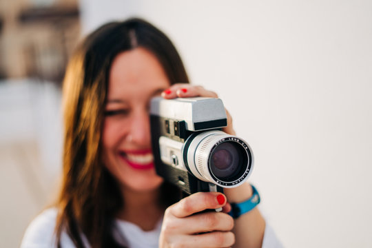 young smiling woman with red lips using a retro video camera isolated on a white background
