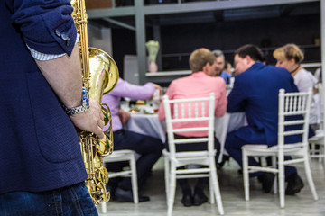 men's hands holding a saxophone on the background of the table with the guests of the restaurant