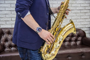 Obraz premium men's hands holding a saxophone against a white wall and a leather sofa