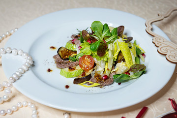 Beef salad with greens and vegetables in a white plate on a vintage tablecloth. Restaurant menu.