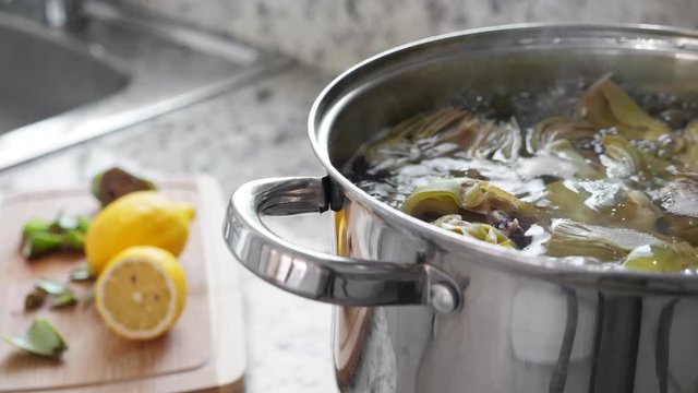 Boiling and cooking artichokes in saucepan, closeup in the kitchen