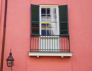 Fototapeta na wymiar Window with with green shutters on salmon colored house in the French Quarter, New Orleans, Louisiana. Small cast iron balcony below window, gas lamp