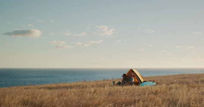 Attractive couple cuddling in comfortable camp site surrounded by golden fields and ocean