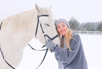Young happy smiling attractive blond woman with horse, overcast winter day