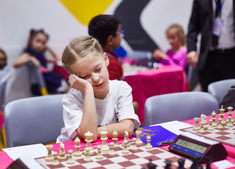Small cute girl infront of chess board on chess tournament look very bored