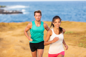 Fit run people couple jogging for fitness running on beach landscape nature outdoors. Woman and man sports athletes training cross-country trail running. Team partners, Asian woman, Caucasian man.
