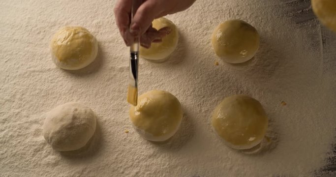 Hand with a brush lubricates dough pies with melange on board filled with flour 4K food cooking video