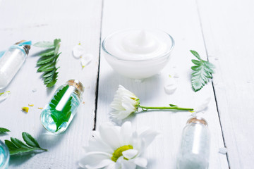 spa setting with cosmetic cream, gel, bath salt and fern leaves on white wooden table background