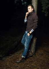 Handsome young man in the forest. A man in warm light poses at night in the woods