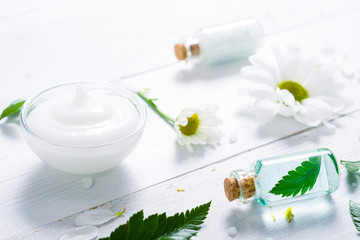 spa setting with cosmetic cream, gel, bath salt and fern leaves on white wooden table background