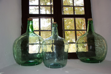 Tres vasijas o tinajas de vidrio o cristal verde, al trasluz de una ventana