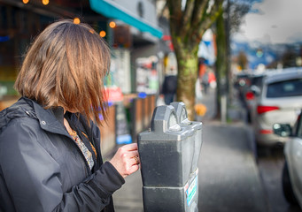 Woman puts money in a parking meter before shopping in local stores