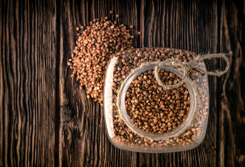 Bank with buckwheat on wooden background. A bunch of buckwheat lies next to the can. View from above.