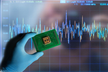 microchip soldered at the board with IC and holded by hand with blue gloves with oscilloscope graph...