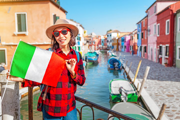 Obraz na płótnie Canvas Young happy traveler with italian flag near famous colorful buildings, Tour and vacation in Italy concept