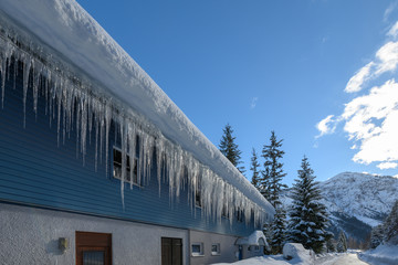 down spout of snowy house roof with lot of icicles at frosty winter