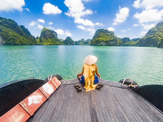 man wearing a Vietnamese hat enjoying the magnifiecent sight of Ha Long bay limestone rocks on a beautiful sunny day during a boat cruise, Vietnam