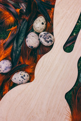Wooden figure of a rabbit and quail eggs on bright feathers background