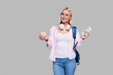 Cost of college education. Portrait of a happy  female student  with piggy bank and cash money in  hands. The girl saves money for training in high school .Neutral grey background. Space for text