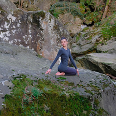 Naklejka na ściany i meble Young slim woman practicing yoga outdoors on big moss rock. Unity with nature concept. Girl in seated spinal twist pose
