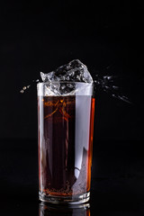 Dropping ice into a glass with a cold drink. Splash of drink in the bar.