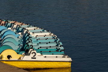 Colorful pedal boats all lined up and floating on the lake. Wide color range boats.