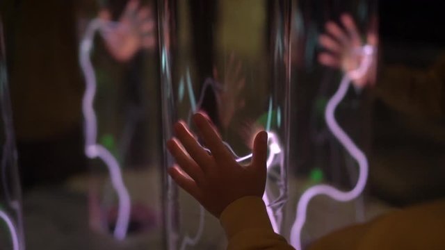 Installation in a science museum. Slowmotion shot of a hand of a woman tauching the tube with glowing gas. inert gas light emission. tube with a glowing plasma