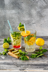 Two glasses of detox water with lemon, kiwi, orange and mint at concrete decorated table background. Concept of healthy lifestyle.