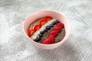 Closeup bowl of healthy oatmeal cereal with strawberry, raspberry, blueberry, mint, chia seeds and coconut isolated at stone textured background.