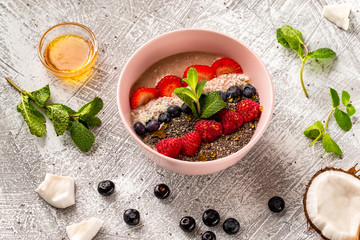 Closeup bowl of healthy oatmeal cereal with strawberry, raspberry, blueberry, mint, chia seeds and coconut at stone table background.