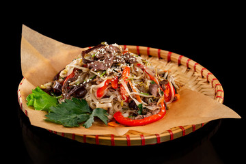 Wicker plate of traditional vietnamese dish - rice noodles with beef meat and vegetables isolated at black background.