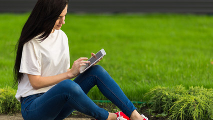 young brunette womanwith tablet serfing in internet on grass