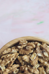 Walnuts kernels, peeled nuts in a wooden bowl on a pink background