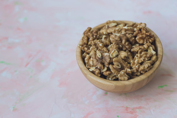 Walnuts kernels, peeled nuts in a wooden bowl on a pink background
