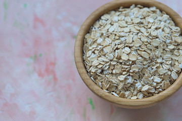 Uncooked oatmeal or oat flakes in a wooden bowl on a pink background