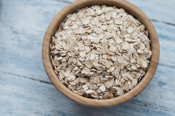 Uncooked oatmeal or oat flakes in a wooden bowl on a blue wooden background
