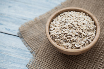 Uncooked oatmeal or oat flakes in a wooden bowl on a blue wooden background