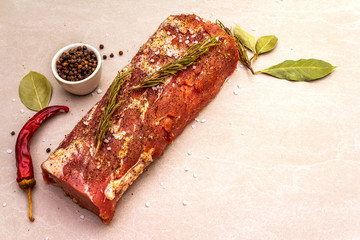 Raw pork loin with species and herbs. Large piece of pickled (marinated) meat on a stone background, close up