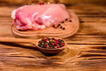 Cutting board with raw chicken fillet and spoon with different spices on wooden table