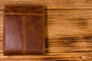 Closed brown leather wallet on wooden table. Top view