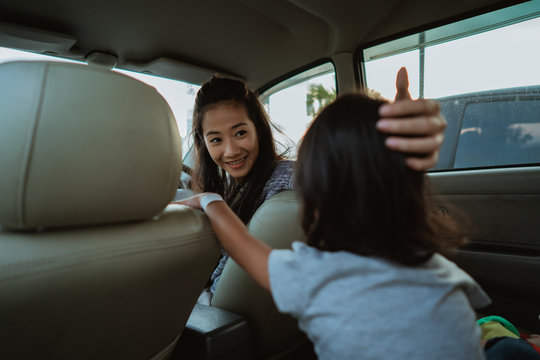 Portrait Of Young Asian Mother Driving A Car And Looking Back At Her Daughter Sitting Behind